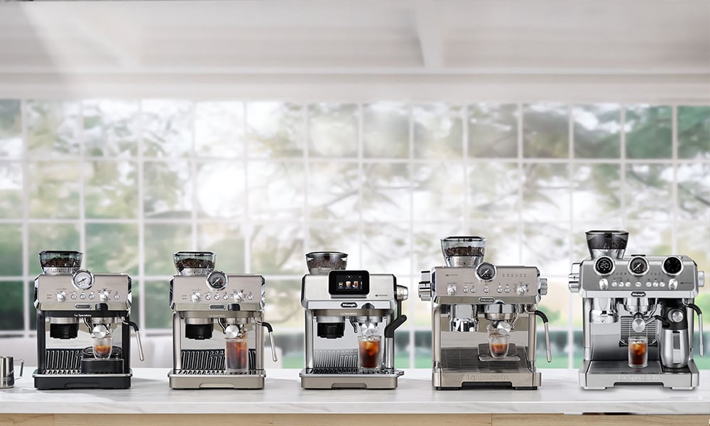 Rząd ekspresów do kawy De’Longhi ustawionych na blacie w jasnej kuchni. - zdjęcie