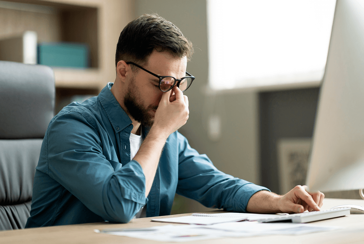 Mężczyzna siedzący przy biurku, trzymający okulary z wyraźnym wyrazem zmęczenia i bólem oczu /Fot. shutterstock